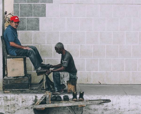 man sitting on stool cleaning shoes at the alley