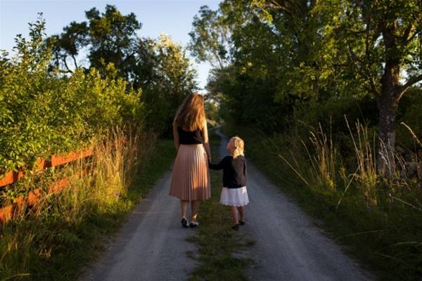 woman and girl walking on road surrounded by green grass